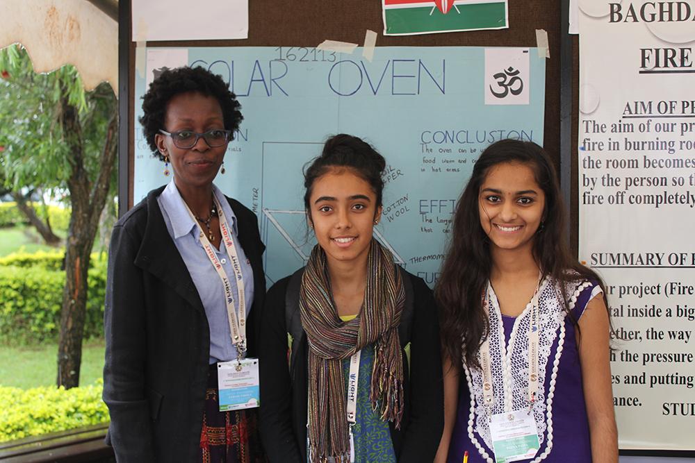 A supervisor with two students at their solar oven project stand